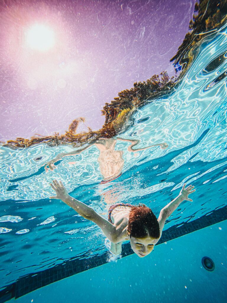Child swimming underwater in a sunlit pool, enjoying a summer day. Bright and joyful scene.