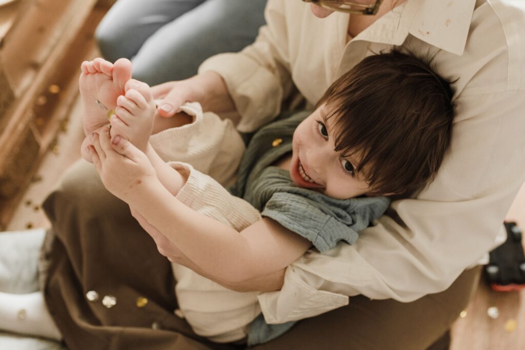 A smiling child enjoying a playful moment while being held by a parent indoors.